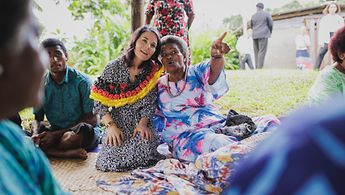 Außenministerin Baerbock sitzt auf einem Teppich und unterhält sich mit einer Frau aus dem Dorf Vuniniudrovo auf Fidschi