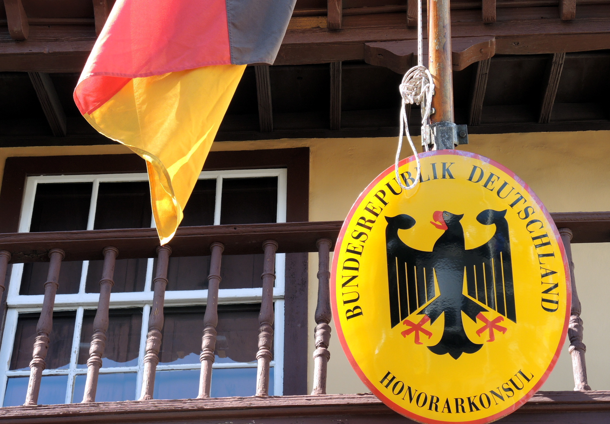 Ein Wappenschild der Bundesrepublik Deutschland macht an einem Gebäude in Santa Cruz de La Palma auf der Kanareninsel La Palma auf das Honorarkonsulat aufmerksam. Eine deutsche Nationalflagge flattert daneben im Wind.